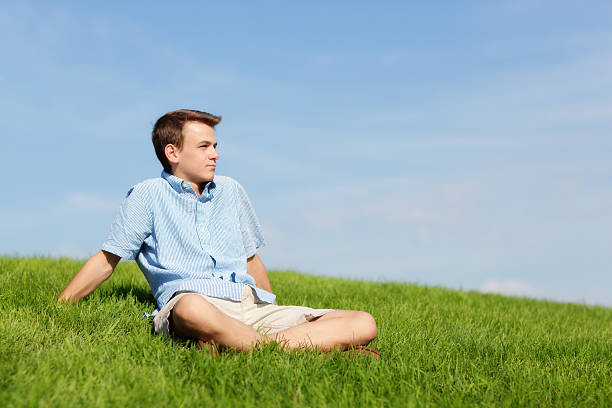 Young Man Sitting Outdoor on Grass Meadow Looking into Future