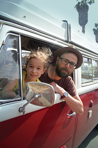 Father and daughter looking out of the window of a old red vintage campervan. Let the adventure begin!