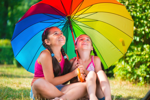 Two happy sisters under colorful umbrella in park
