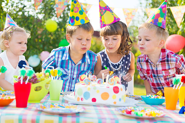 Kids blowing candles on cake at  birthday party stock photo