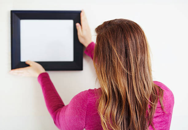 Hanging your copyspace Rearview shot of a young woman putting up a picture frame adjusting photos stock pictures, royalty-free photos & images