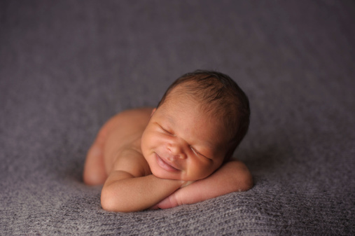 An adorable newborn sleeping with a smile on his face.