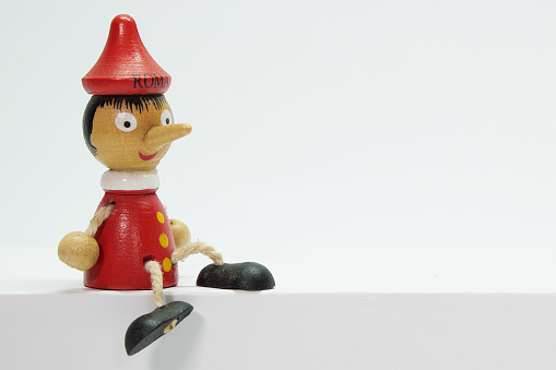 Pinocchio, wooden toy representing a long-nosed boy, sitting on a plain, isolated white background.