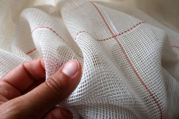 white coarse cotton or linen curtains made of weaves of thin threads. a woman's hand is feeling the fabric. window decoration room. red stripe. the fabric is folded in soft waves. apartment interior. - burlap canvas home decorating color image imagens e fotografias de stock