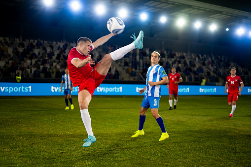 Male football player kicking ball during match on sports field, wide shot