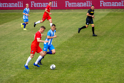 Male soccer players running and leading ball during match on sports field, full length shot