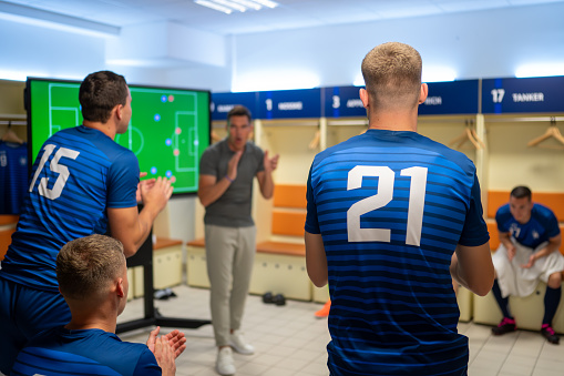 Male soccer coach planning game strategy and motivating team in locker room