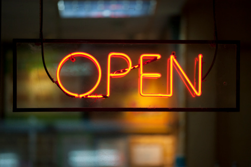 Close up on an orange neon light shaped into the word “open” inside a black rectangle. The background behind is totally blur, yet, we can guess that it is a shop or a restaurant with a low lightning.