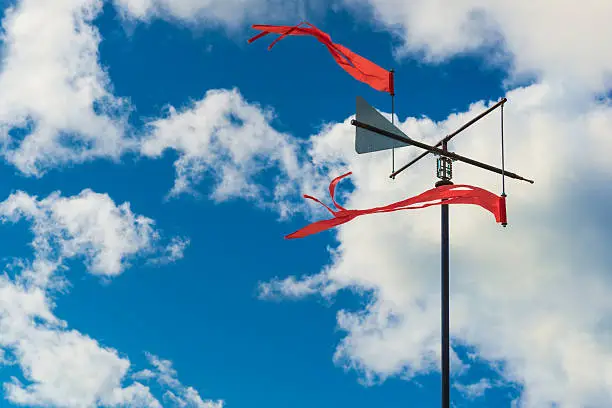 Simple windvane on sky background with white clouds.