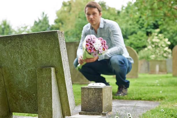 istock Man Placing Flowers By Headstone In Cemetery 186593700