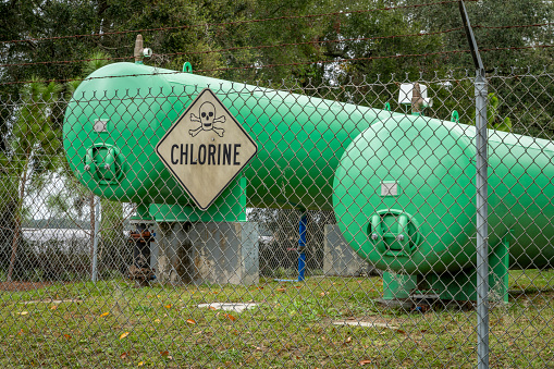 industrial chlorine gas tanks behind a fence with a warning sign
