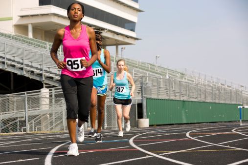 Three women run track during competitive event.  Selective focus on middle runner's jersey.