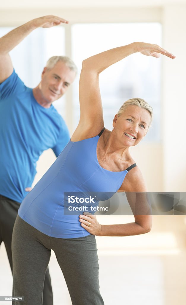 Couple Doing Stretching Exercise At Home Active senior couple doing stretching exercise at home 60-64 Years Stock Photo