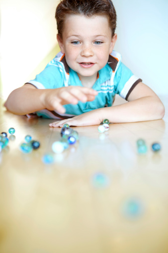 A cute little boy reaching for his marbles on the floor at home