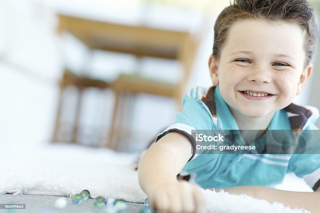 Having fun with marbles A cute little boy reaching for his marbles on the floor at home 6-7 Years Stock Photo