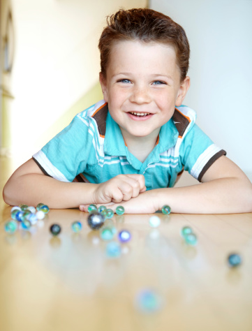 A cute little boy lying on the floor playing with marbles at home