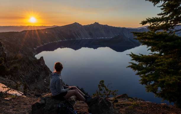 夏にクレーターレイクに沈む夕日を見るために座っている女性 - crater rim ストックフォトと画像