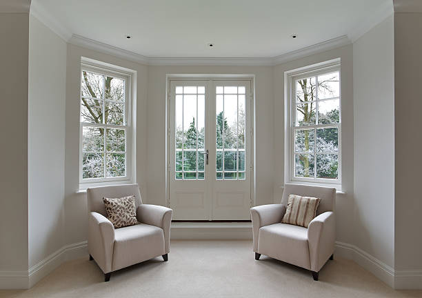 bay window and frosty view a bay window area in the bedroom of a luxury mansion home with two arm chairs and silk cushions. Two doors provide access to a small balcony. The view through the Georgian style white wooden windows are towards a frosty garden in the Winter, with green conifers. The lighting of the image is distictly "wintery".  bay window stock pictures, royalty-free photos & images