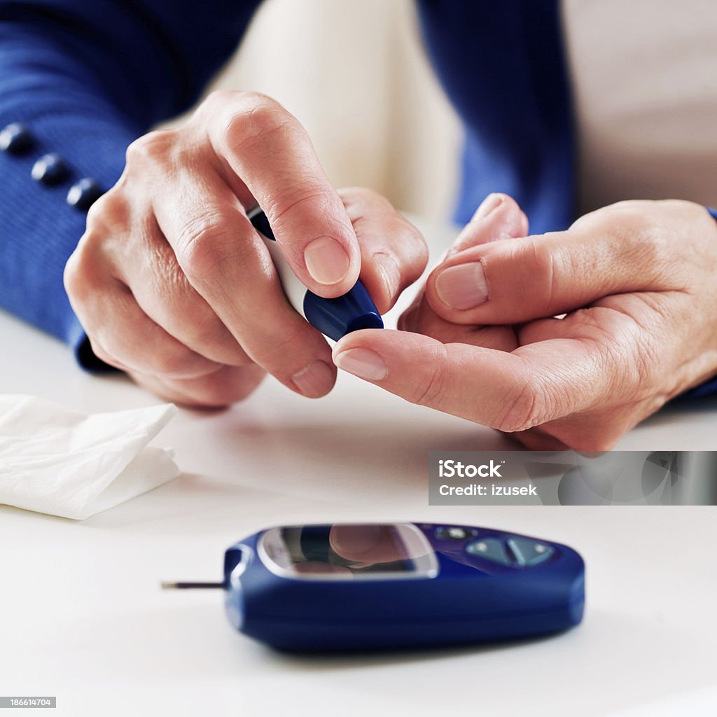 Woman checking glucose level Close up of mature woman's hands doing a glucose level finger blood test. 60-64 Years Stock Photo