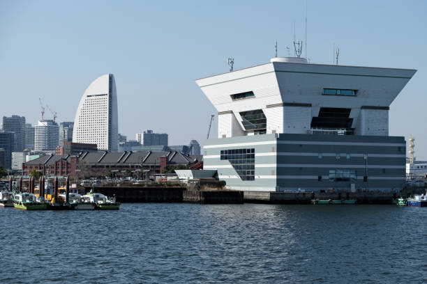 Boats moored at Port of Yokohama with the Cruise ship Terminal building. In the distance, the Yokohama Red Brick Warehouse, a historical building that is used as a complex that includes a shopping mall, banquet hall, and event venues. The complex was originally used as customs buildings and is located at the Port of Yokohama in Naka-ku, Yokohama, Kanagawa, Japan.