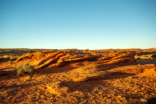 Barren rugged desert landscape with textured stones. This remote and barren desert landscape make a nice nature background. The orange and red hues are amplified taken in the early morning sun. The tall shadows enhance the texture. There are small green scrubs that makes this look like an alien landscape.