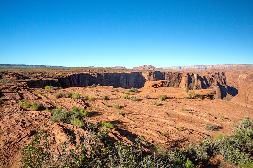 Beautiful and Rugged landscape of the Arizona desert - in the foreground you can see small desert shrubs and then a large gorge . Taken near horseshoe bend, this extreme terrain is both beautiful and majestic. The steep cliff in the middle has the Colorado river at the bottom. A scenic travel tourism photo.