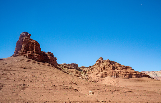 Rugged sand stone structure near Marble Canyon in the Arizona Desert. The rough terrain make rough cliff faces. The valley has been eroded over the years and makes a dramatic landscape. There are small green arid shrubs in the foreground with a deep blue cloudless sky in the background with plenty of copy space. A nice travel and tourism nature landscape.