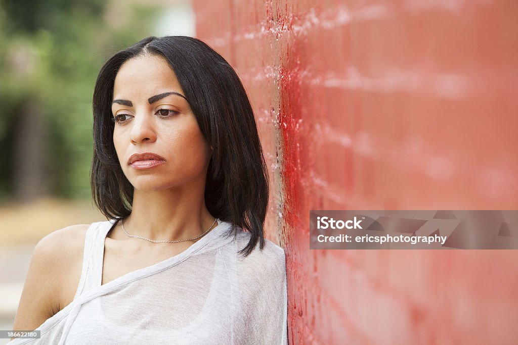 Looking away Portrait of a Hispanic woman in her 20s standing by a red, brick wall. Females Stock Photo