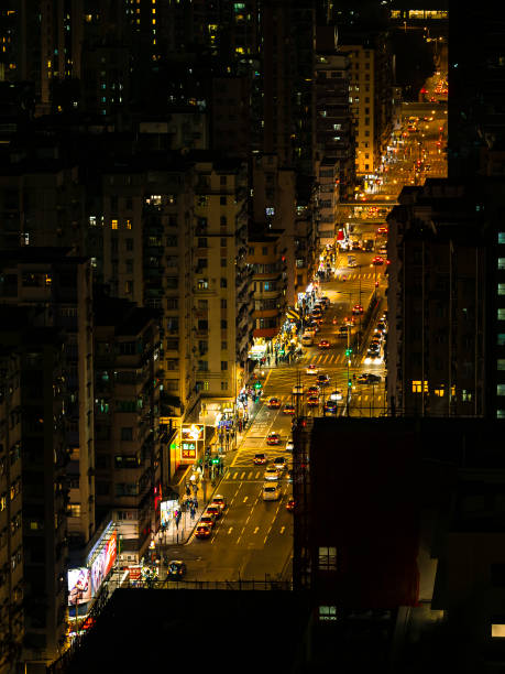The scene captured from the summit of Garden Hill in Hong Kong showcases the vibrant bustle of nighttime activity in the Sham Shui Po District, with a tapestry of bustling traffic and crowds weaving through the streets below.