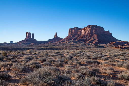 Tall spires and mesas of rich dark red rugged sandstone mountains near Monument Valley in Arizona and Utah of western USA in North America. This is part of the Navajo Native Indian Nation in USA.  Nearest cities are Phoenix and Grand Canyon Arizona, Salt Lake City, Utah, Denver and Durango, Colorado.