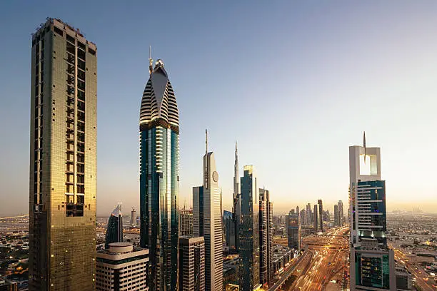 Modern Urban Skyscrapers illuminated in the Financial Downtown District of Dubai. Landmarks like Dubai Metro, the Burj Khalifa Tower and Burj Al Arab Hotel are visible. Long Exposure, Motion Blurred Car Lights. Dubai, United Arab Emirates.