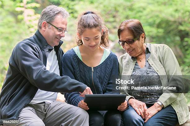 Multigeneracional Grupo Mirando A La Computadora Tablet In Park Foto de stock y más banco de imágenes de Adolescencia