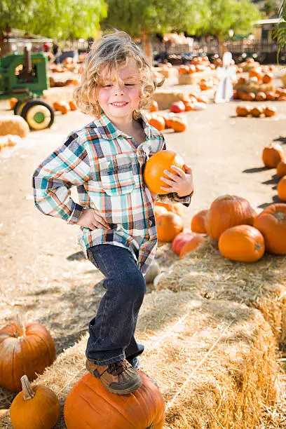 Adorable Little Boy Sitting and Holding His Pumpkin in a Rustic Ranch Setting at the Pumpkin Patch.