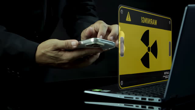 Businessman using laptop and smartphone with radioactivity sign symbol on a computer screen. Science, danger icon, x-ray dangerous, cyber war and warning on virtual screen. Radiation hazard concept.