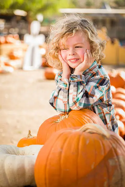 Adorable Little Boy Smiles While Leaning on a Pumpkin at a Pumpkin Patch in a Rustic Setting.