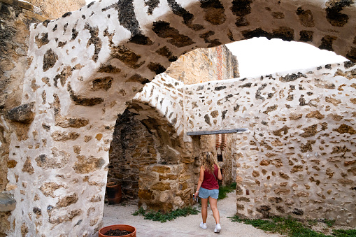 Female tourist walks under arched passageway leading to the chapel at Mission San JosÃ©, built in 1720, known as the Queen of the Missions in the historical park, San Antonio, Texas, USA