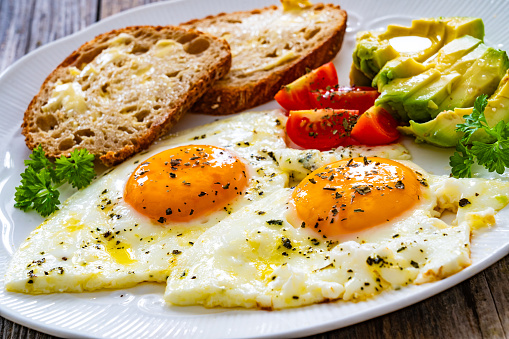 Continental breakfast -   fried eggs with fresh avocado and tomatoes on wooden table