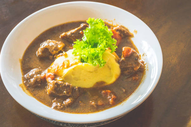 A plate of beef stew with green beans, broccoli, squash, onion and mashed potato.