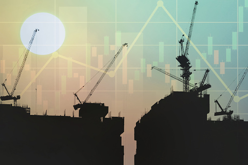 Image of tower crane  working on top of the  buildings with graph, chart and candlesticks data for stock business and construction industry presentation background.