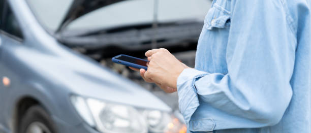 istock breakdown, broken car, repair. Woman uses mobile phone check insurance premiums through application due to car accident . Find garage to get car fixed during country tour, waiting for help, emergency. 1866592995