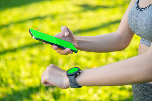 Close up side view green screen of Asian Woman Analyzing Smartwatch Data During Leisure Exercise in a Public Park, Utilizing Technology for Health