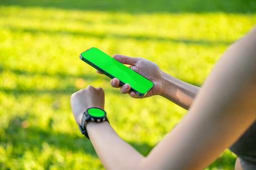 Close up side view green screen of Asian Woman Analyzing Smartwatch Data During Leisure Exercise in a Public Park, Utilizing Technology for Health