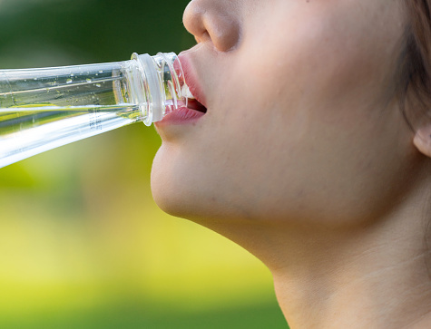 Close up, focusing on the mouth of a Young Asian Woman Enjoying Hydration and Relaxation After Exercise in a Public Park