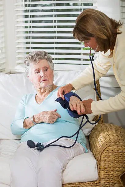 Caregiver (60s) checking blood pressure of elderly woman (90s).  Main focus on elderly woman.