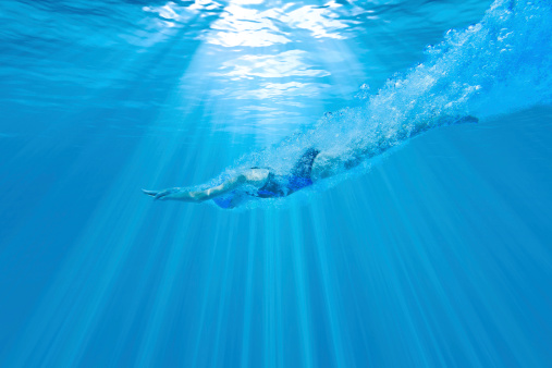Underwater photograph of a female swimmer diving into the water with the sun beaming above