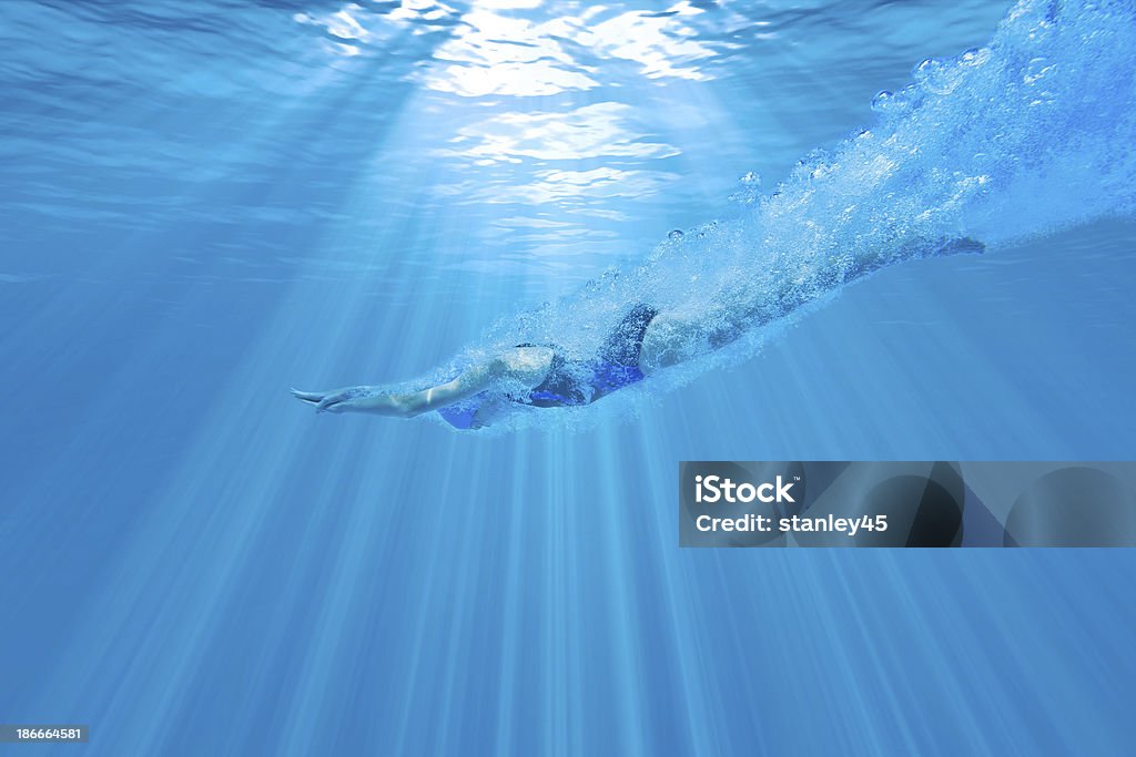 Girl Diving Underwater with Perfect Form Underwater photograph of a female swimmer diving into the water with the sun beaming above Diving Into Water Stock Photo