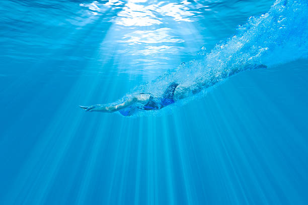Girl Diving Underwater with Perfect Form Underwater photograph of a female swimmer diving into the water with the sun beaming above diving into water stock pictures, royalty-free photos & images