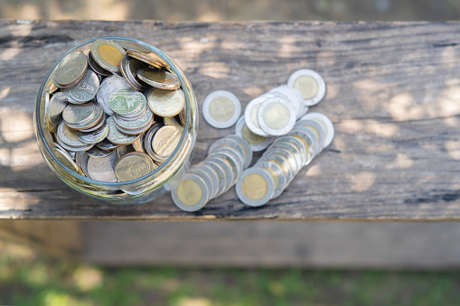 Saving money coins in jug glass on the old wooden tabel concept finance and saving. Thai coins, selective focus.