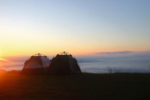 two tents for camping on top of mountain with sea of mist and sunshine in the morning.