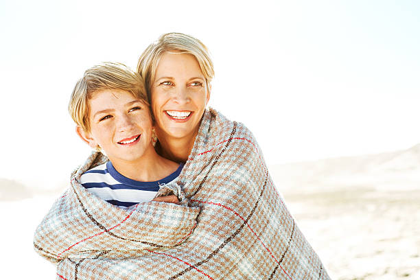 istock Woman With Blanket Embracing Son From Behind At Beach 186667198